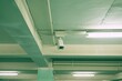 © Victor Bertrand - A wall-mounted security camera in an industrial-looking parking garage, illuminated by sterile lighting, keeps a watchful eye on the vehicles and the space.