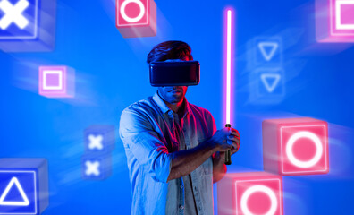 Energetic man with VR glasses fencing neon sword with music block. Professional gamer playing a game while holding sword and enter in metaverse with blue background. Blurring background. Deviation.