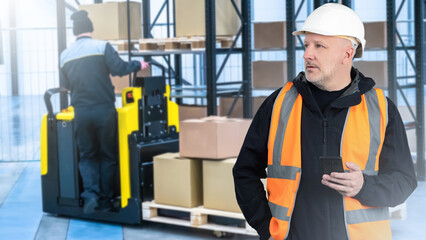 Poster - Man warehouse manager. Storage supervisor. Businessman stands inside logistics warehouse. Forklift with pallet behind storekeeper. Warehouse manager holding phone. Man storekeeper wearing orange vest