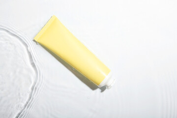 Poster - Cosmetic product. Tube with cream in water on light background, top view