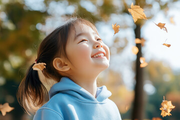 Wall Mural - Chinese little girl smiling wearing sweatshirt playing at sunny autumn park