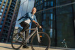 © muse studio - A man rides his bicycle through an urban business district, smiling confidently in the sunlight.