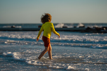 Wall Mural - Carefree child running on sea. Happy cute child running near ocean on warm summer day. A Cute little kid boy running and splashing in sea or ocean on a family vacation. Kid running along the beach.