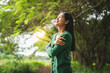 © Phushutter - confident asian woman embraces self-love, standing peacefully in serene park at sunset. joyful smile, she enjoys fresh air, breathing deeply, radiates calm and positivity in tranquil surroundings.