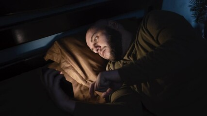 Tired man lying in bed sleepless holding smartphone in hand scrolling social media, suffer sleep disorder in dark bedroom. Man need rest. anxiety, sleeplessness and depression concept