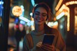 © Ahmed - Cheerful pretty young woman in cool eyeglasses and trendy wear walking on metropolis street with night lights enjoying online playlist songs in earphones and reading sms with good news on smartphone