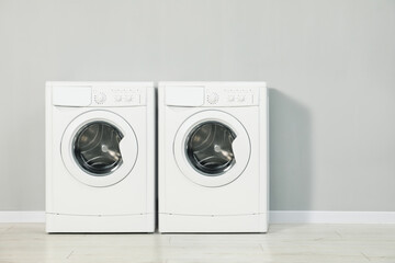 Two washing machines near light grey wall