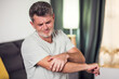 © Aleksej - Man With Pain In Elbow. Pain relief concept. Middle age man feeling the pain in hand elbow at home. Male touching his painful elbow