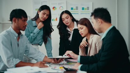 Wall Mural - Team of marketing professionals gathered around a table, engaging in a brainstorming session while reviewing financial data displayed on a tablet