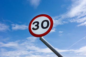 A speed limit sign with the number 30 against a clear blue sky.