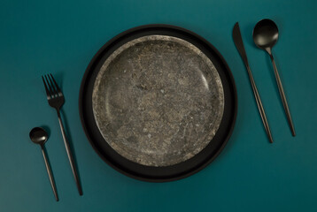 Top view of brown marble plate, black plate and cutlery on dark green background. Food presentation, stone tray. Table setting, copy space, flat lay.