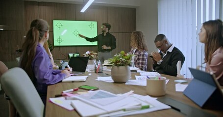 Wall Mural - Young professional giving a business presentation to diverse colleagues in a modern conference room. Team members taking notes and discussing strategies.