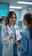© Juan Mari - Smiling female doctor gives a thumbs-up while discussing patient care with a nurse in a modern hospital. Great for healthcare marketing, medical blogs, and promoting teamwork in medical settings