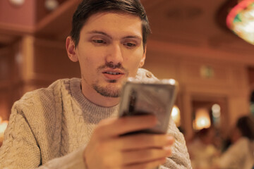 Portrait of a young guy with a phone sitting at the table.