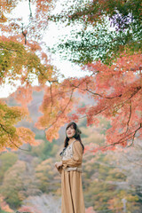 Poster - A woman stands gracefully among vibrant autumn leaves, showcasing beauty of nature. warm colors of fall create serene and picturesque backdrop