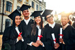 © HBS - Portrait of beautiful smiling graduates celebrating graduation and holding certificates with academic goals achieved. Successful studies and a bright future.