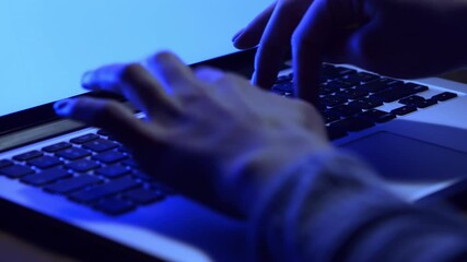Poster - A person types on a laptop keyboard, illuminated by a blue light in a dark environment, focusing intently on the screen.