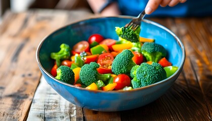 Wall Mural - Vibrant salad preparation with fresh broccoli, juicy cherry tomatoes, and crisp bell peppers in a blue bowl on a rustic wooden table