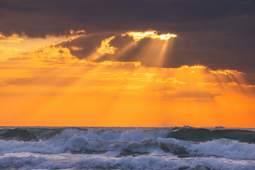 Wall Mural - beautiful sunrise over the sea splashing waves, sun rays through dramatic morning clouds, scenic lan