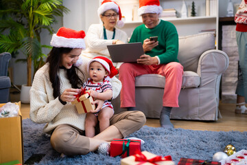 Asian family on Christmas Day. Everyone is happy together in a Christmas themed room filled with presents and orange lights.