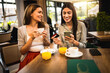 © Mediteraneo - Two girl best friends met at the cafe to shop online together. They are using mobile phone and credit card. Friends hang out and drink coffee and orange juice.