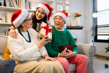 Asian family on Christmas Day. Everyone is happy together in a Christmas themed room filled with presents and orange lights.