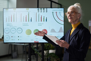 Poster - Elderly woman presenting detailed business data analysis on digital screen with various charts and graphs for customer satisfaction, employee satisfaction, and continued growth