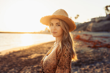 Wall Mural - Portrait of one young beautiful woman on the sand of the beach enjoying and relaxing at the sunset of the day. Looking at the camera serious..