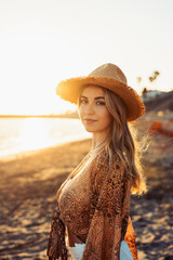 Wall Mural - Portrait of one happy beautiful woman on the sand of the beach enjoying and having fun at the sunset of the day. Looking at the camera smiling..