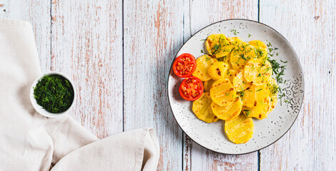 Golden sliced grilled potatoes with herbs on a plate on the table top view web banner