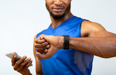 Aufkleber - Fitness Tracker. Portrait of afro muscular man holding mobile phone and looking at smartwatch, yellow wall, copyspace