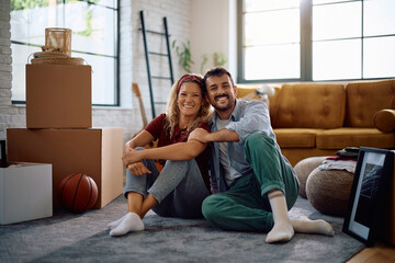 Happy couple relaxing on floor at their new house and looking at camera. Copy space.