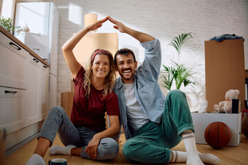 Happy couple showing home symbol with their hands while moving into new house.