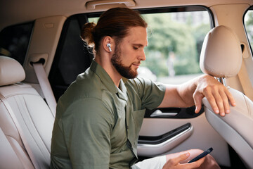 Young man using smartphone with wireless earbuds in a modern car interior