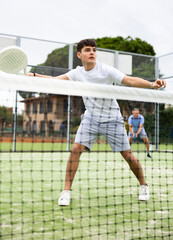 Wall Mural - Sportive young man playing padel together with a partner. View through the tennis net