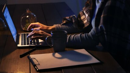 Poster - A person works on a laptop in low light, with a mug and notepad nearby, creating a cozy atmosphere.