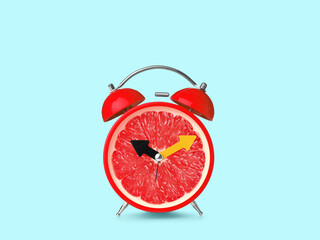 Poster - Juicy grapefruit on alarm clock dial against light blue background. Creative poster