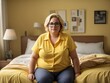 © shrinay - plus size senior female in yellow shirt  sitting on bed in bedroom