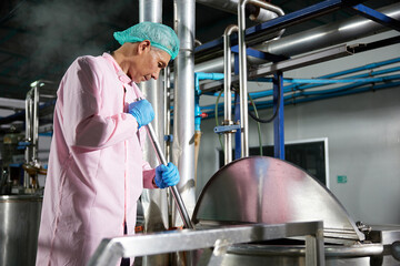 worker stirring water on large industrial pot in the factory