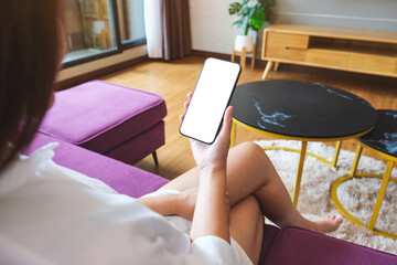 Wall Mural - Mockup image of a woman holding mobile phone with blank desktop white screen at home