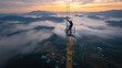 © busro - Brave Technician working on Telecommunication Tower in Remote Mountain Village Aerial View