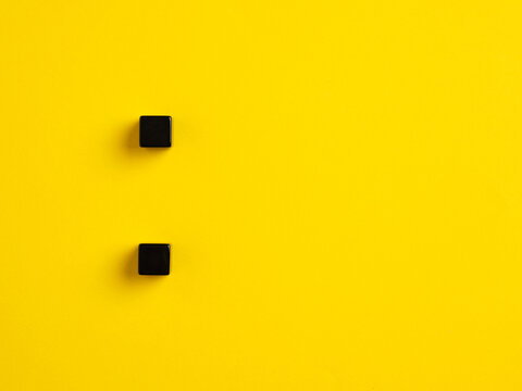 The colon symbol punctuation mark. Two black cubes on yellow background.