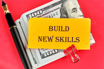 Business, education build new skills concept. Copy space. Concept word BUILD NEW SKILLS on yellow paper on dollar bills on a red background