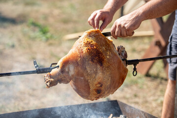 A person is cooking a large piece of meat on a spit