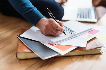 Wall Mural - Close up of man writing notes in planner, working at desk from home. Telecommuting and home office.