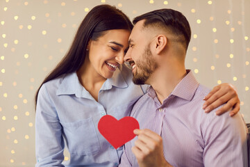 Young happy couple in love holding red paper heart, Saint Valentine's Day celebration, hug cuddle, lovers enjoy tender romantic moment, harmonic relationships, showing loving care, sincere feeling