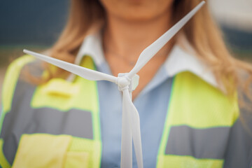 Poster - A Female Engineer is proudly Holding a Miniature Wind Turbine Model while standing on a busy Construction Site, highlighting her commitment to engineering, innovation, sustainability, and teamwork