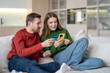 © DimaBerlin - Happy family couple online shopping at home sits on comfortable couch using phone and bank card. Interested satisfied woman holding smartphone making internet purchases with man husband. Black Friday.