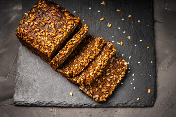 Rye flour bread with sunflower seeds, sliced on a black mica board on a dark background. High quality photo