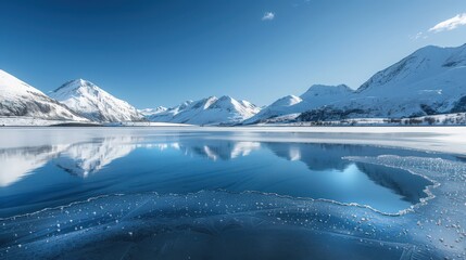 Canvas Print - A stunning snowscape showing a frozen lake surrounded by snow-capped mountains, with a clear blue sky reflecting off the ice.